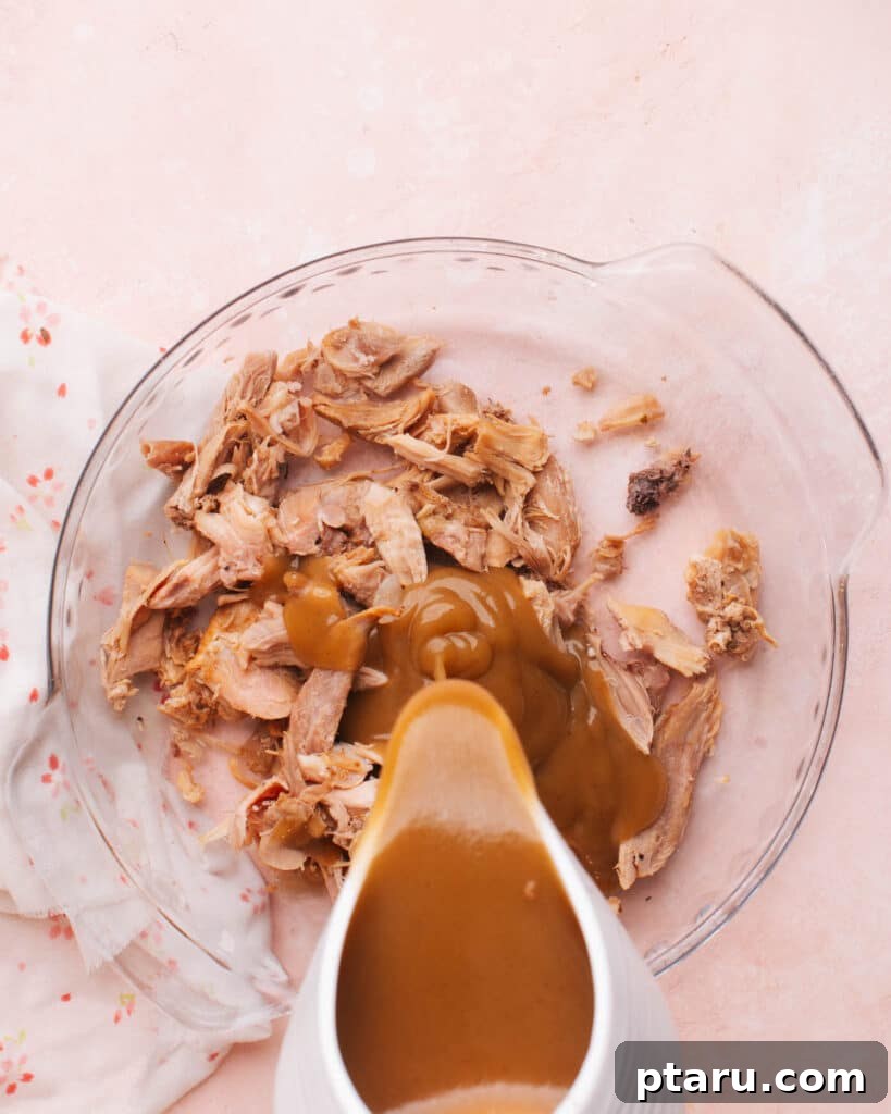 Thanksgiving Revival Casserole 5 Pouring rich, homemade gravy over shredded leftover turkey in a mixing bowl, ready for the casserole filling.
