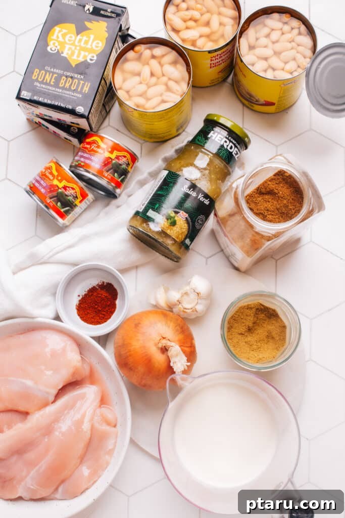Guilt-Free White Chicken Chili 3 A flat lay of fresh ingredients for healthy white chicken chili, including chicken breasts, onions, garlic, various spices, canned green chiles, white beans, milk, and corn, ready for cooking.