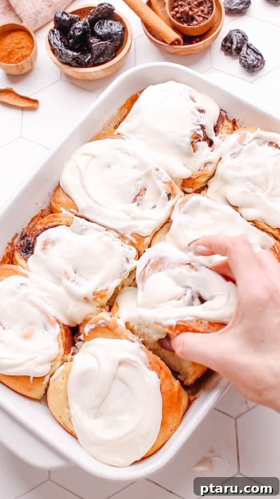 Sweet Cinnamon Raisin Swirls 10 Someone pulling out a soft cinnamon raisin roll covered in cream cheese frosting with tongs.
