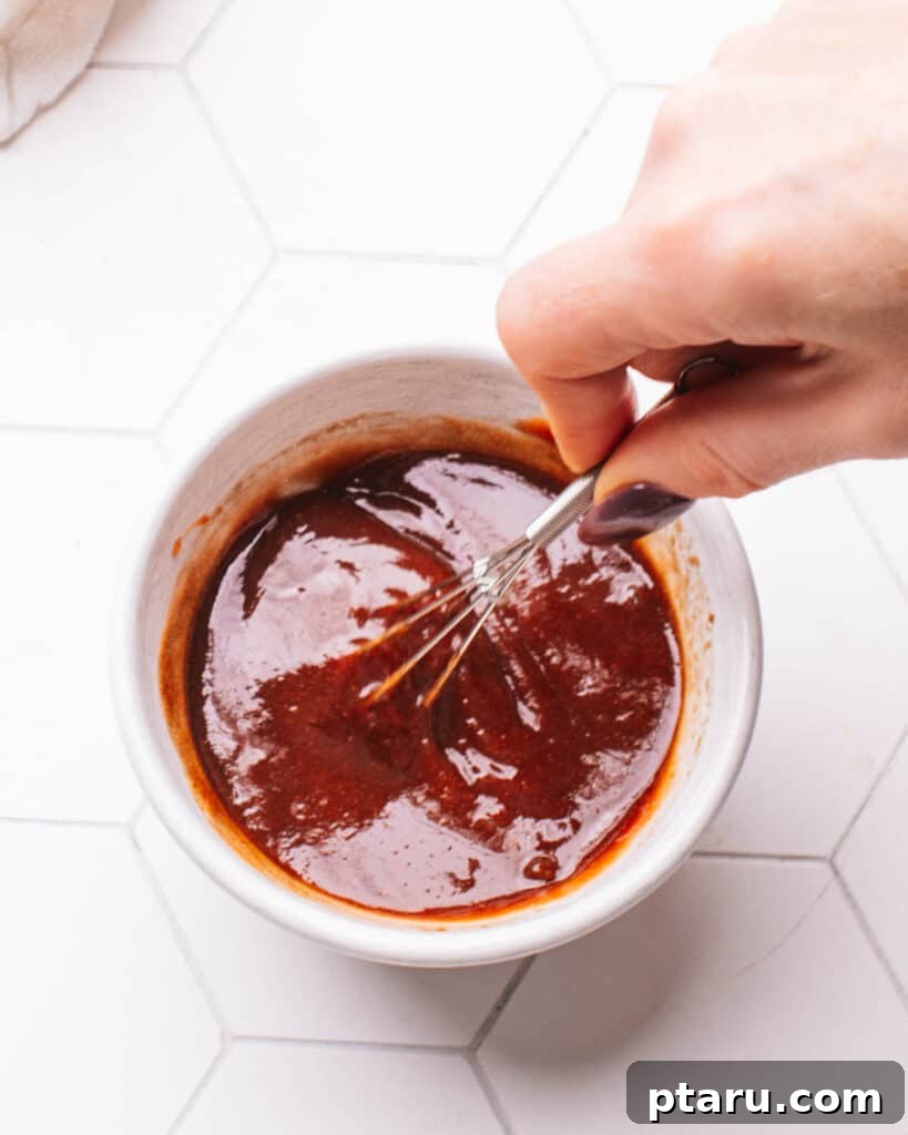 Foolproof 3 Ingredient Meatloaf Glaze 5 A hand whisking the meatloaf glaze ingredients in a small bowl, showing the smooth consistency.