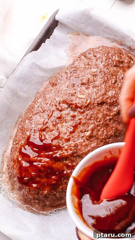 Foolproof 3 Ingredient Meatloaf Glaze 7 Applying the meatloaf glaze generously over the surface of a partially baked meatloaf using a pastry brush.