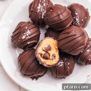 Cookie dough bites covered in chocolate in a pile on a plate. The top one has a bite taken out.