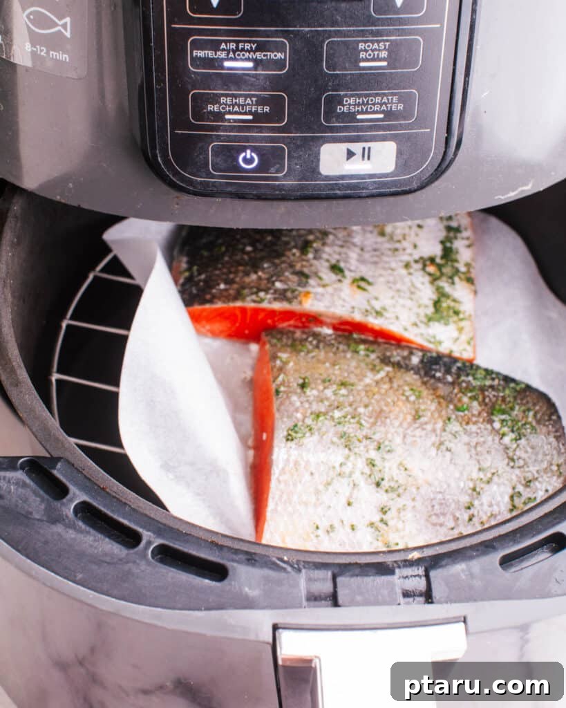 Perfectly Moist Flaky Air Fryer Frozen Salmon 5 Hands carefully placing a seasoned frozen salmon fillet into an air fryer basket.