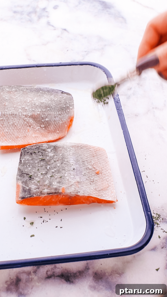 Perfectly Moist Flaky Air Fryer Frozen Salmon 6 Close-up of a hand sprinkling salt and other seasonings onto a frozen salmon fillet.