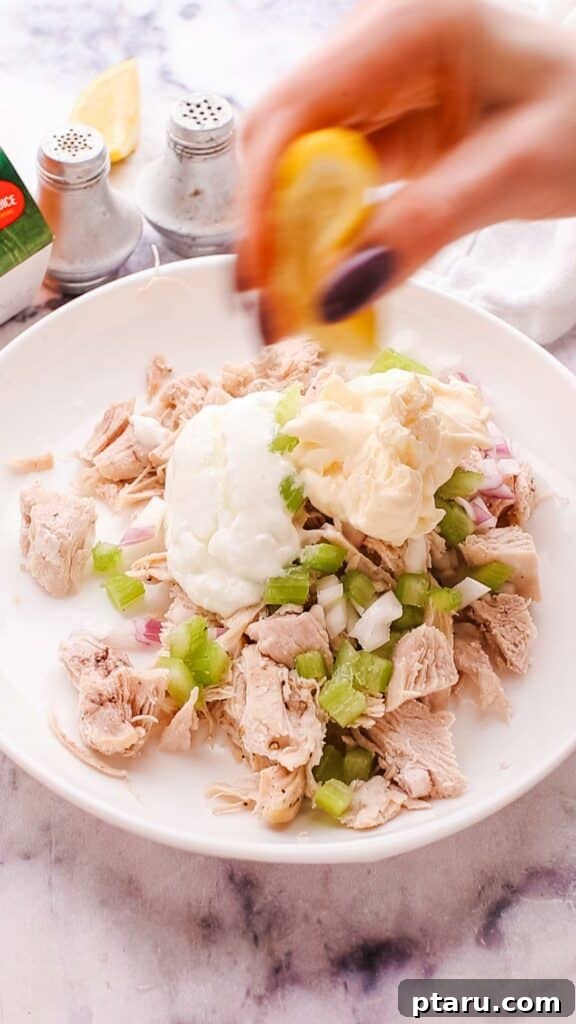 Flavorful Curried Chicken Salad with Sweet Grapes 6 A hand squeezing fresh lemon juice into a bowl of chicken salad, adding a bright and zesty flavor.