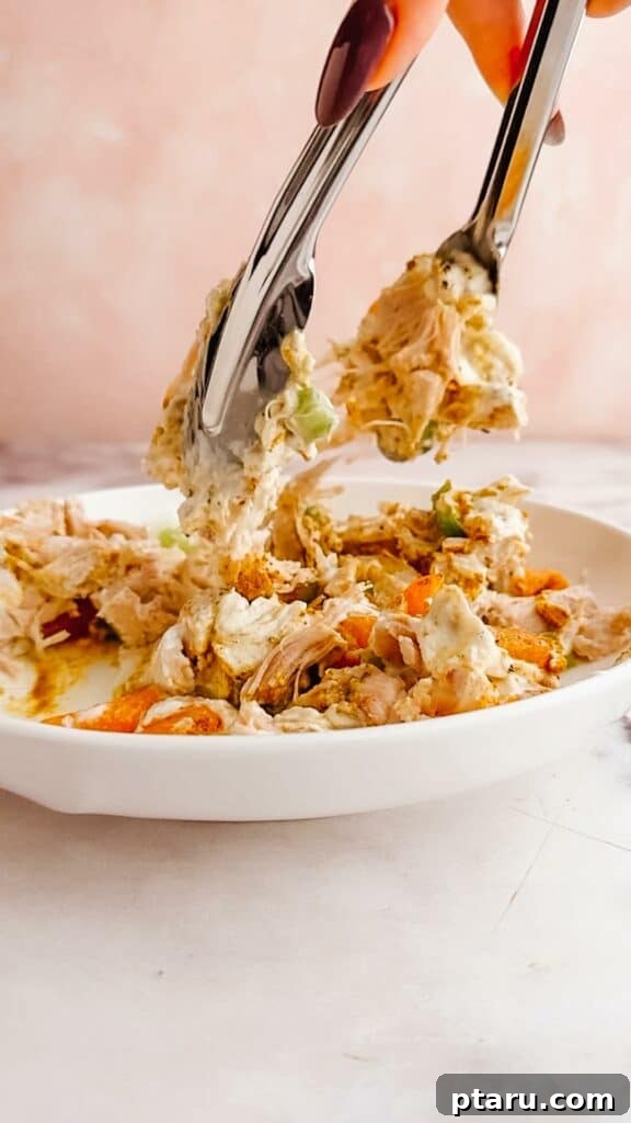Flavorful Curried Chicken Salad with Sweet Grapes 8 A spatula stirring all the ingredients in a large bowl, combining the chicken, dressing, grapes, and celery to create a cohesive salad.