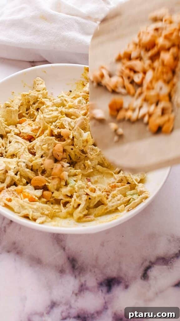 Flavorful Curried Chicken Salad with Sweet Grapes 9 A hand adding toasted nuts, such as almond slivers or cashews, as a final crunchy topping to the curry chicken salad.