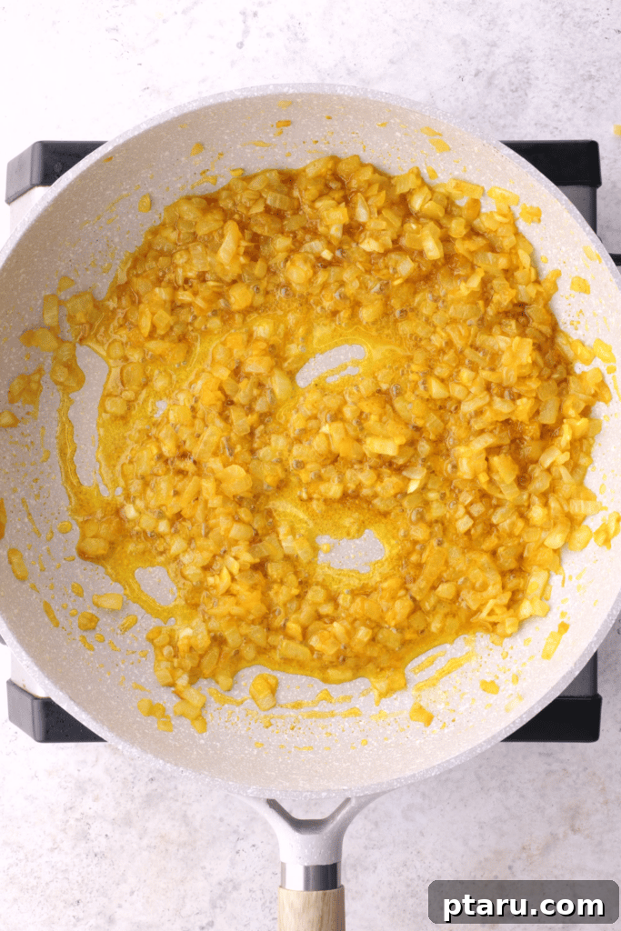 Golden Samosa Bake 4 Finely chopped onions are sautéing in a large pan, slowly caramelizing to a rich golden brown, which is the foundational step for the Samosa Pie filling.