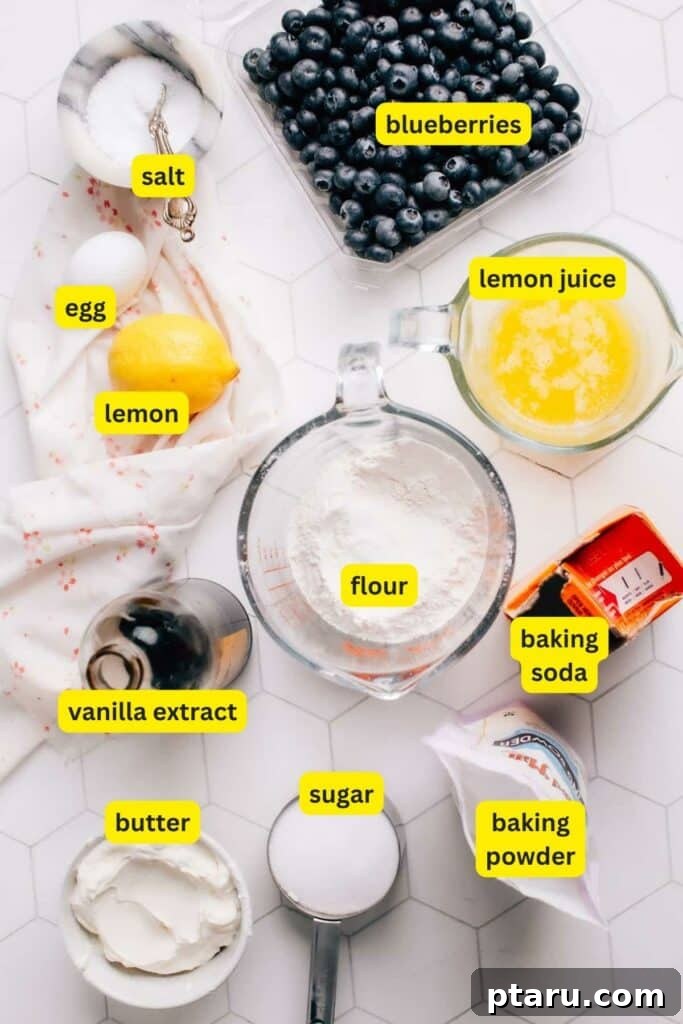 Creamy Lemon Blueberry Muffins 3 A selection of fresh ingredients including flour, sugar, baking powder, baking soda, salt, melted butter, sour cream, vanilla extract, an egg, lemons, and fresh blueberries, all neatly arranged on a kitchen countertop.