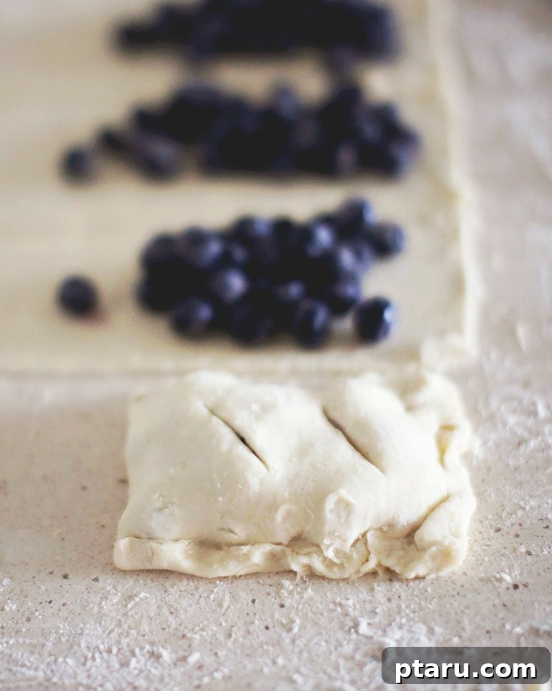 Homemade Blueberry Pocket Pies 4 A batch of freshly baked blueberry hand pies, some with icing drizzled over them.