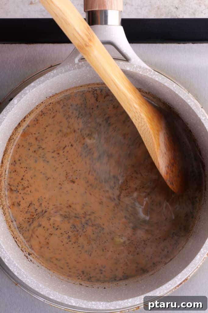 Secrets to Authentic Indian Masala Chai 5 Stirring the black tea into the milk and spice mixture as it brews in a saucepan for homemade chai.