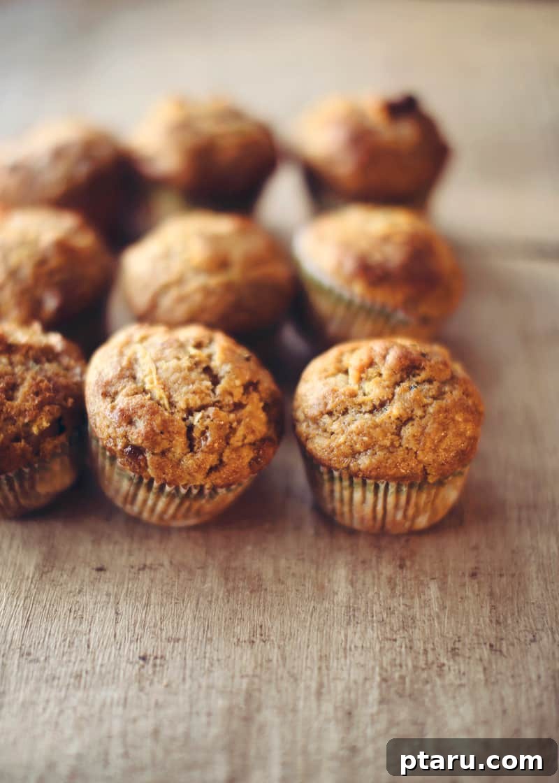 Tender Spiced Pumpkin Zucchini Muffins 2 Freshly baked Pumpkin Zucchini Muffins on a wooden table, garnished with a sprinkle of cinnamon.