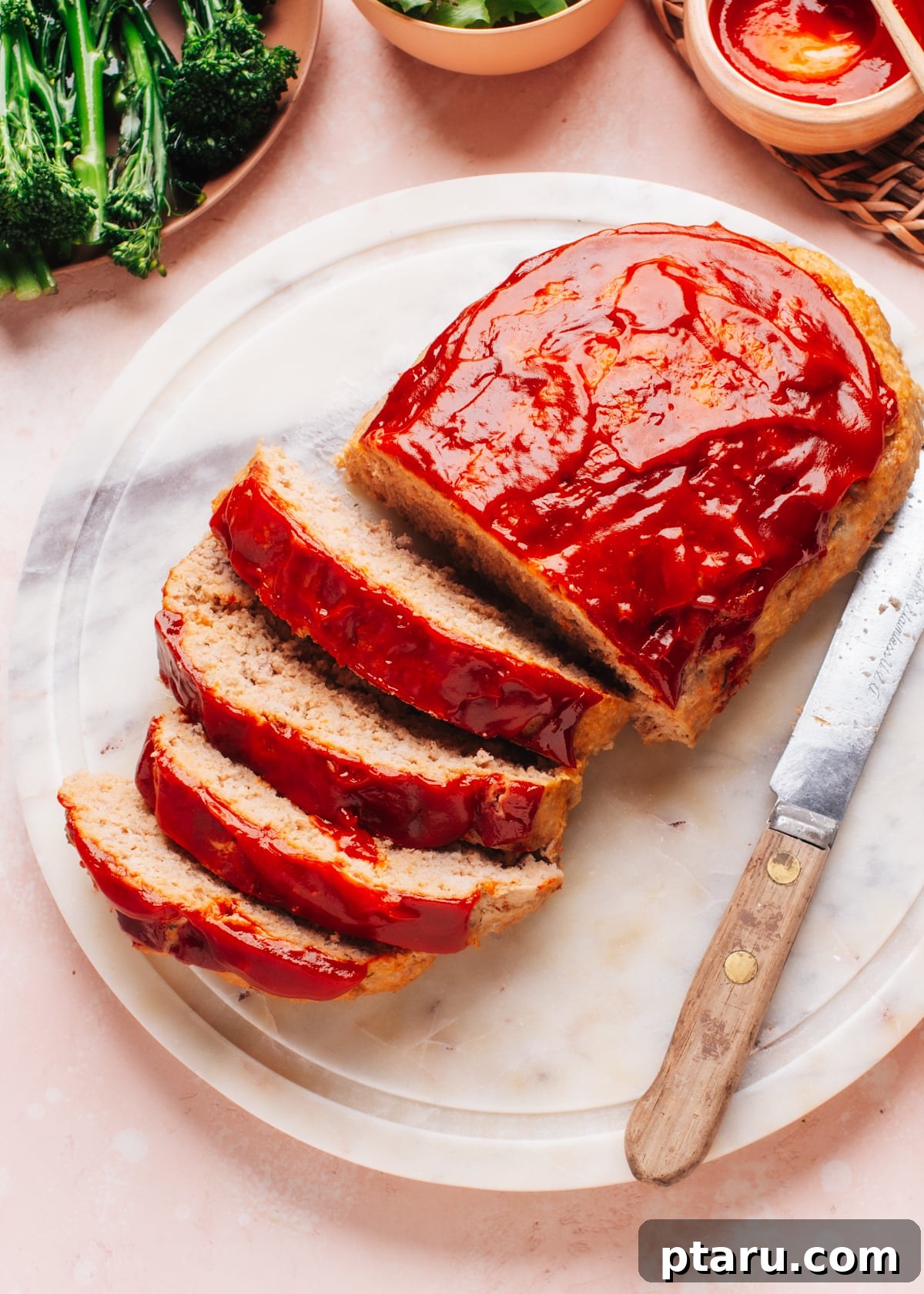 The Ultimate Juicy Turkey Meatloaf 8 A thick slice of moist turkey meatloaf on a white plate, with a knife and fork beside it, ready to be enjoyed.
