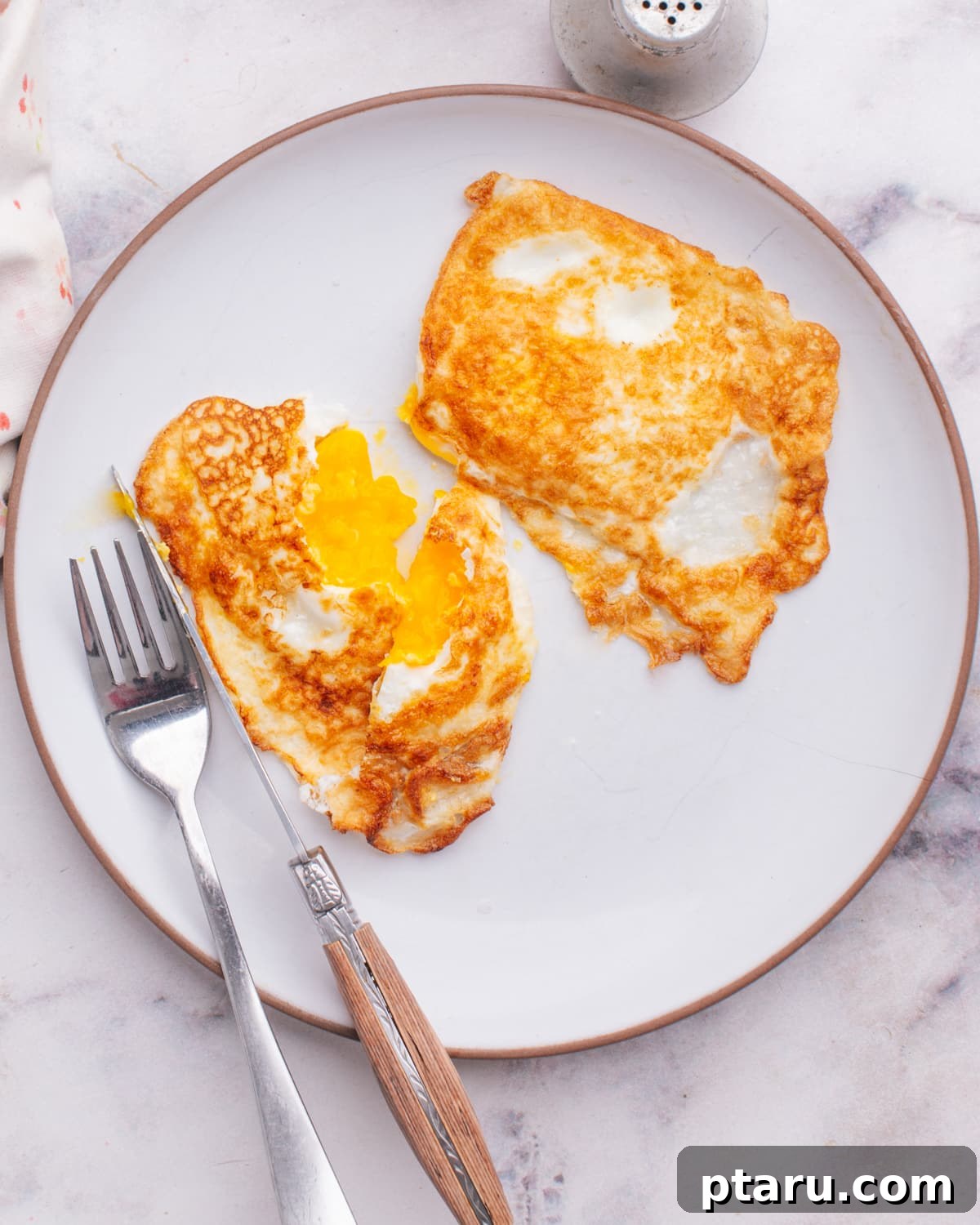 Foolproof Over Medium Eggs 2 Eggs over medium on a plate with knife and fork, ready to be enjoyed.