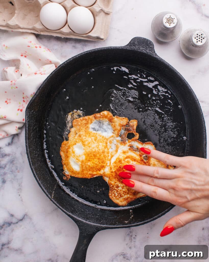 Foolproof Over Medium Eggs 6 A hand gently touching an over medium egg in a pan to test its doneness.