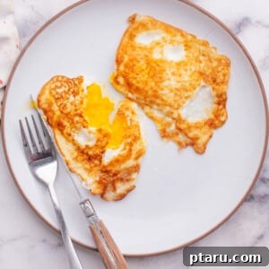 Eggs over medium on a plate with knife and fork.