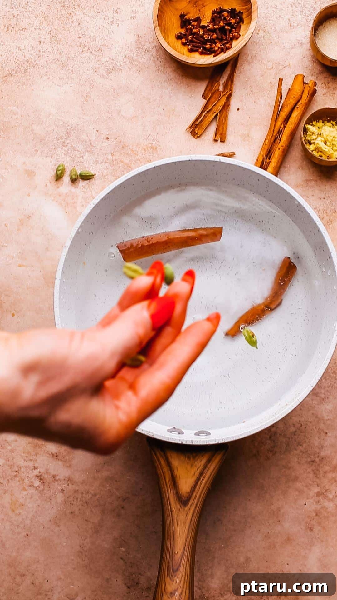 Perfectly Spiced Iced Chai Latte Made Easy 5 Adding green cardamom pods to a pot of water for infusing spices, a crucial step in preparing the authentic chai concentrate, with steam gently rising.