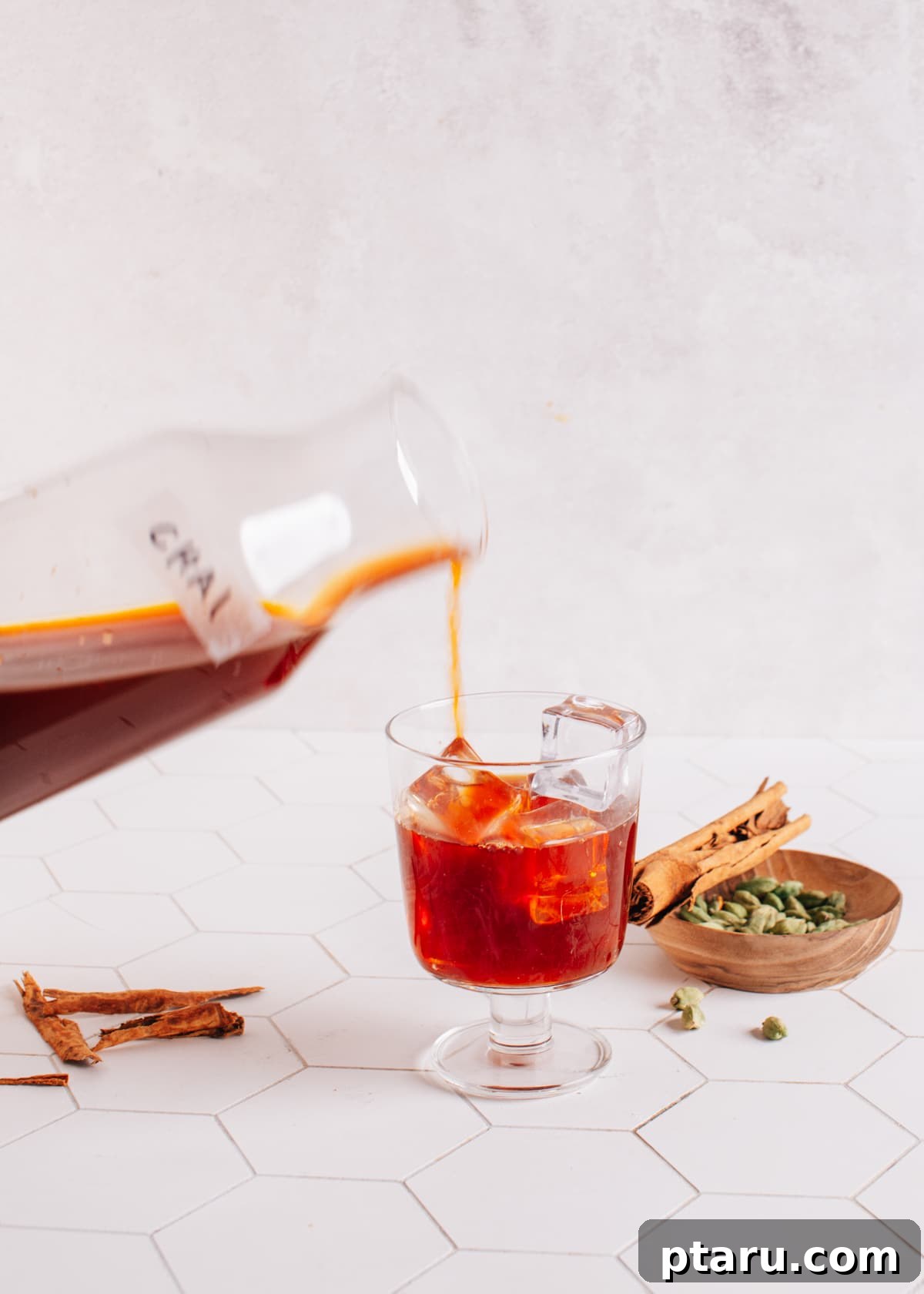 Perfectly Spiced Iced Chai Latte Made Easy 8 Pouring the rich, dark chai concentrate over ice in a tall glass, forming the base layer for a homemade iced chai latte, with milk soon to be added.