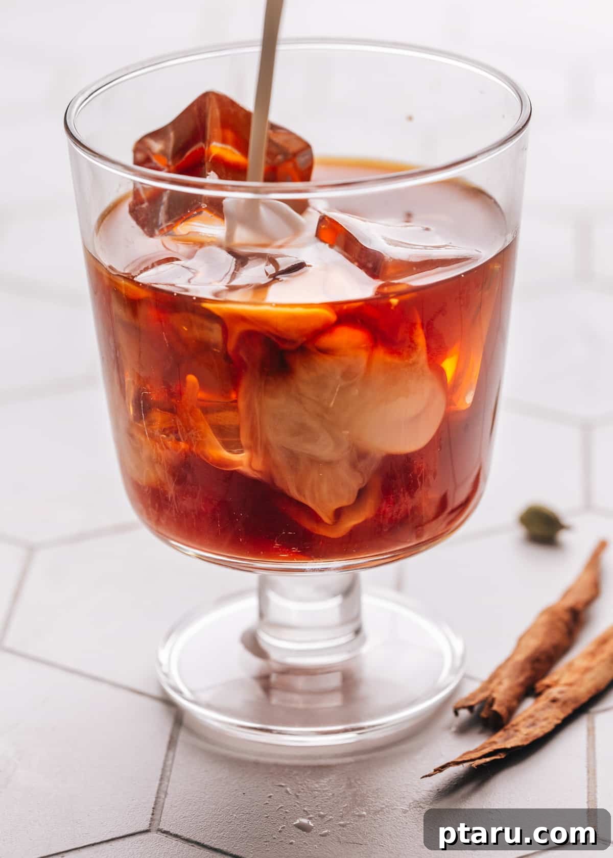 Perfectly Spiced Iced Chai Latte Made Easy 9 Fresh, creamy milk being poured gracefully into a glass of already poured iced chai latte, creating a beautiful swirl of creamy white against the dark, spiced tea base.