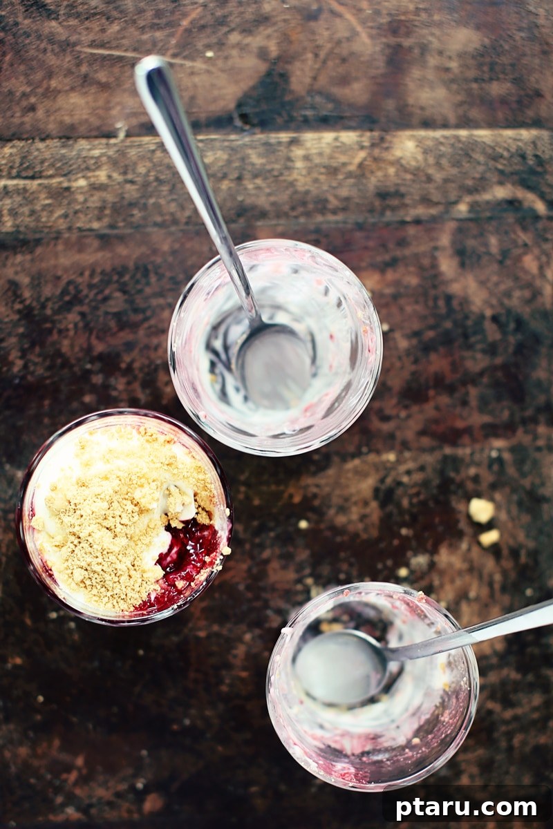 Effortless Raspberry Cheesecake Cups 3 Close-up of No-Bake Raspberry Cheesecake Parfaits showing distinct layers of cream, raspberries, and graham cracker crumbs in a glass