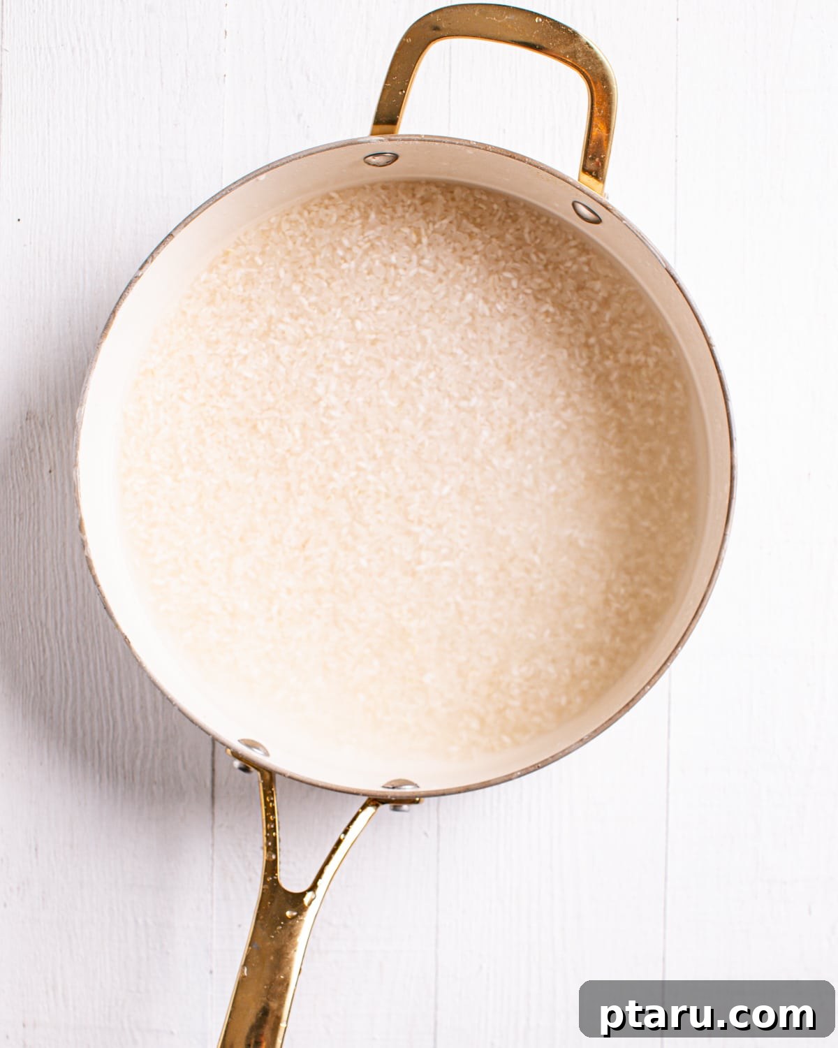 Viral TikTok Sushi Bake 4 Uncooked sushi rice being held in a saucepan, ready for rinsing and cooking, with a clean kitchen background.