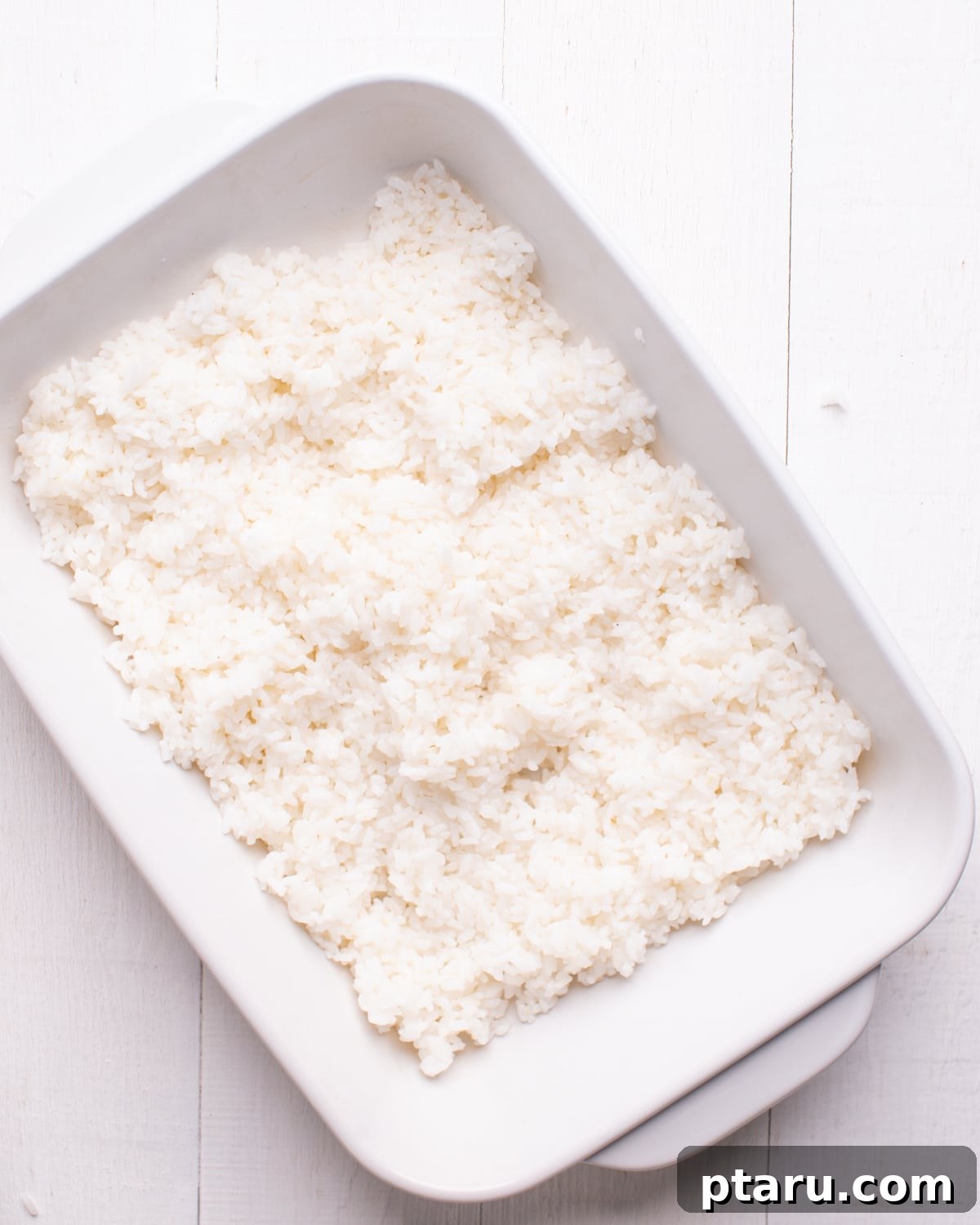 Viral TikTok Sushi Bake 5 Cooked and seasoned sushi rice spread evenly in a baking dish, forming the base of the sushi bake.