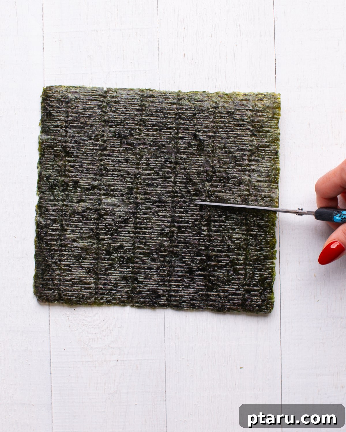 Viral TikTok Sushi Bake 7 A hand cutting crispy nori seaweed sheets into smaller squares, ready to be served alongside the sushi bake.