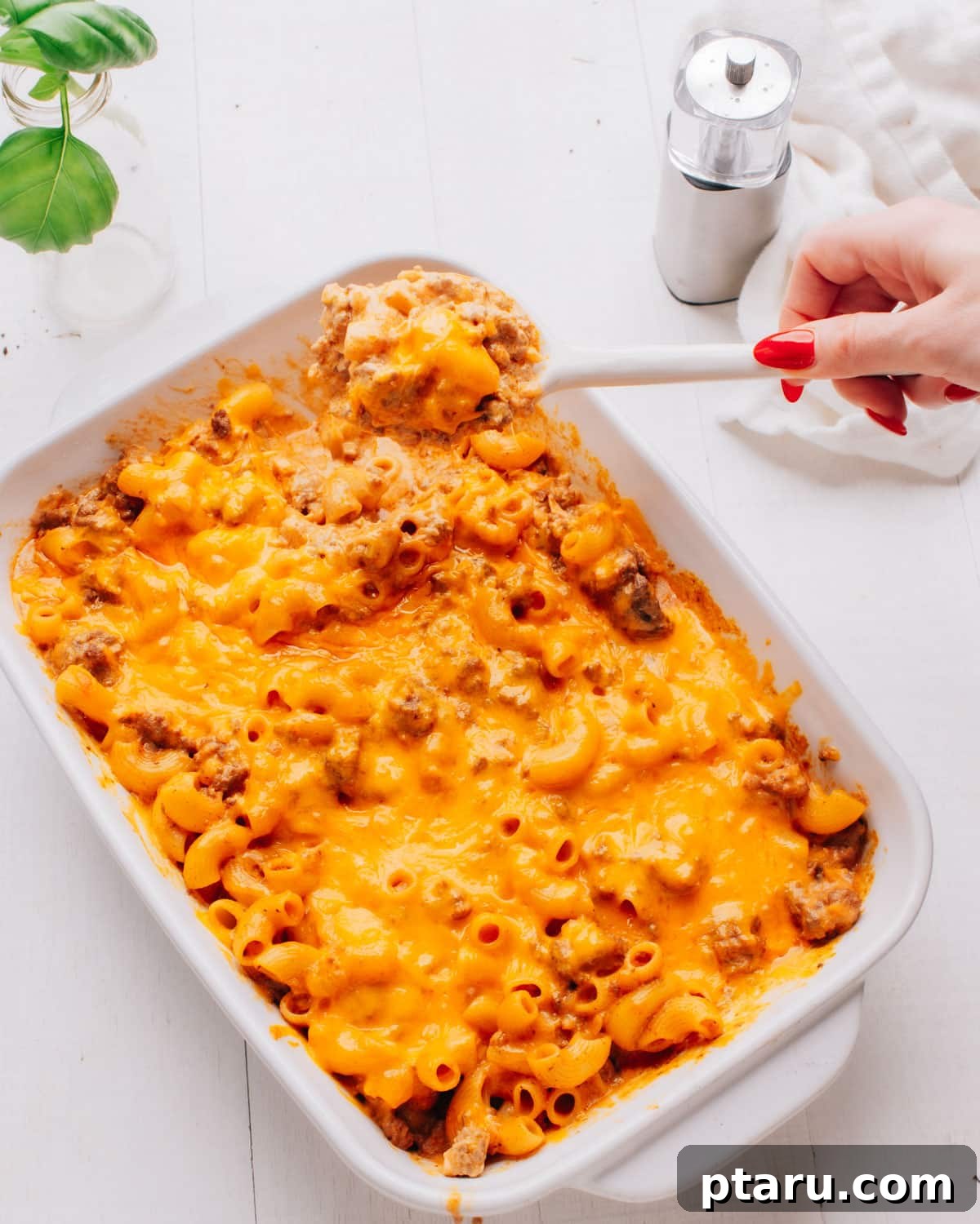 No-Fuss Cheeseburger Dinner 7 Lifting a spoonful of cheeseburger casserole. A hand holding a spoon with a hearty serving of cheeseburger casserole, showing the cheesy top and macaroni inside.
