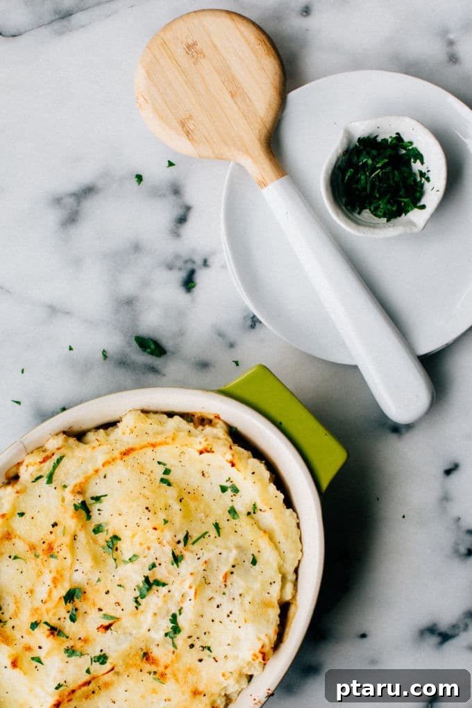 Hearty Lentil Shepherd's Pie 5 A beautifully finished, golden-brown vegetarian shepherd's pie with lentils, generously sprinkled with vibrant fresh parsley, rests invitingly next to a stack of clean plates, ready to be served as a comforting meal.