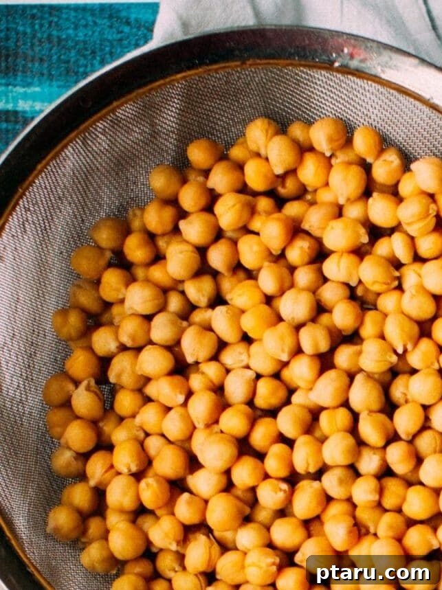 Indian Masala Chickpea Curry 3 Soaked chickpeas in a strainer, with small bowls of various Indian spices like cumin, garam masala, and cinnamon on the side, ready for cooking.