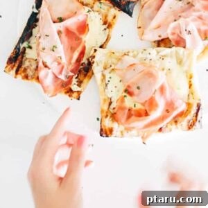 A close-up view of a single grilled puff pastry tart, showcasing the melted Gruyere cheese, ham, and fresh chives.