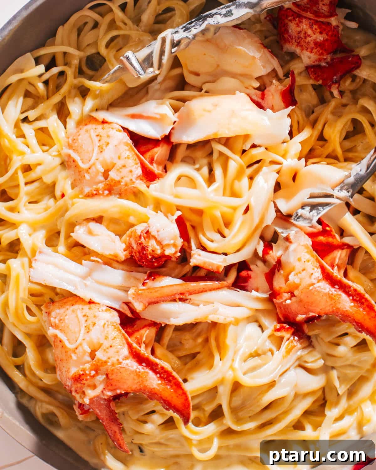 Decadent Lobster Pasta with White Wine Cream 2 Lobster Pasta Recipe in a pan with tongs, showcasing a vibrant and rich dish.