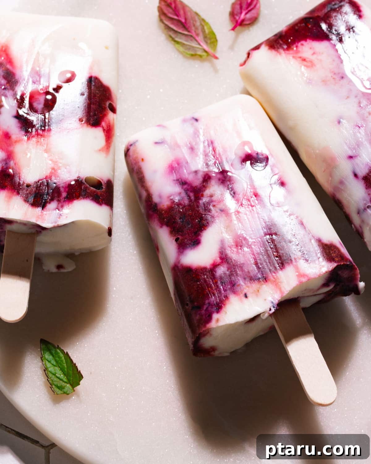 Easy 5-Minute 3-Ingredient Yogurt Popsicles 2 Yogurt Popsicles on a plate, showcasing their creamy texture and vibrant berry swirls.