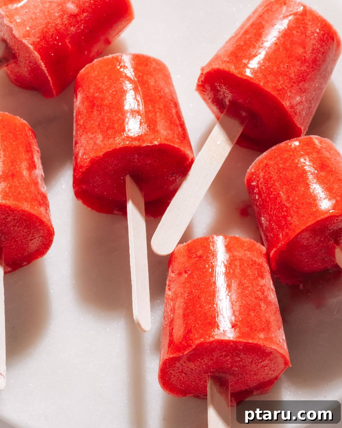 Effortless Three Ingredient Strawberry Pops 3 Close-up of strawberry popsicles arranged neatly on a white plate, highlighting their smooth texture and rich color.
