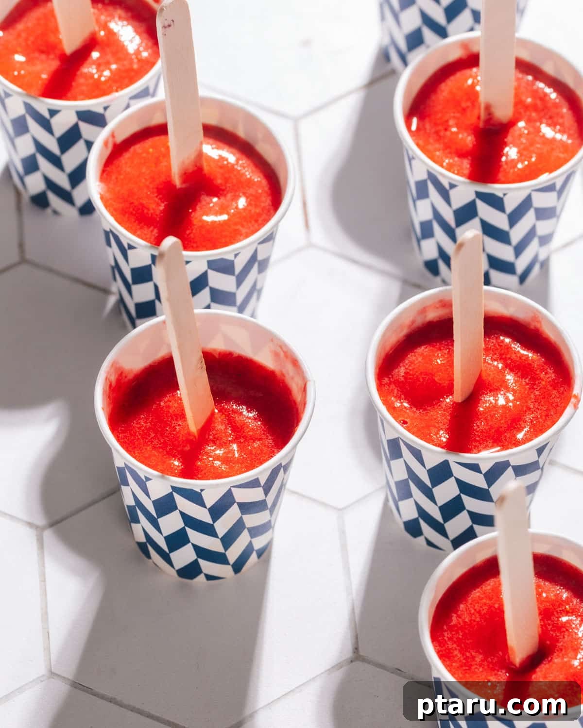 Effortless Three Ingredient Strawberry Pops 7 Individual strawberry popsicles served in small paper cups, ready to be enjoyed.