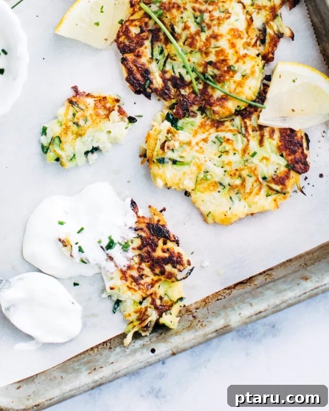 Golden Zucchini Cakes 4 Three golden zucchini fritters on a wooden board, accompanied by a small bowl of creamy dip and fresh chives for garnish.