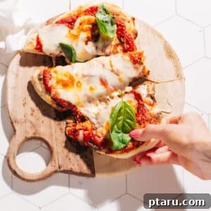 A hand pulling a slice of freshly baked Naan Pizza from the baking tray.