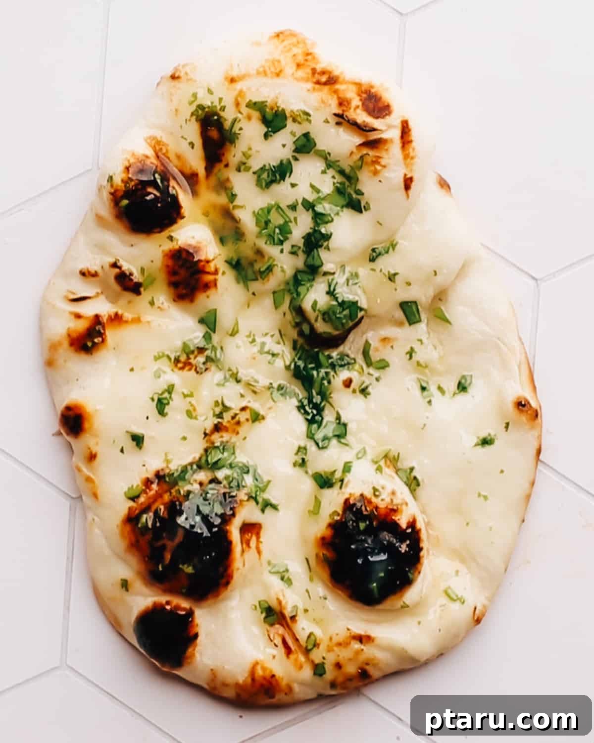 Unbelievably Soft Stretchy Garlic Naan 2 Freshly baked homemade garlic naan bread glistening with butter, arranged beautifully on a rustic kitchen countertop, ready to be served.
