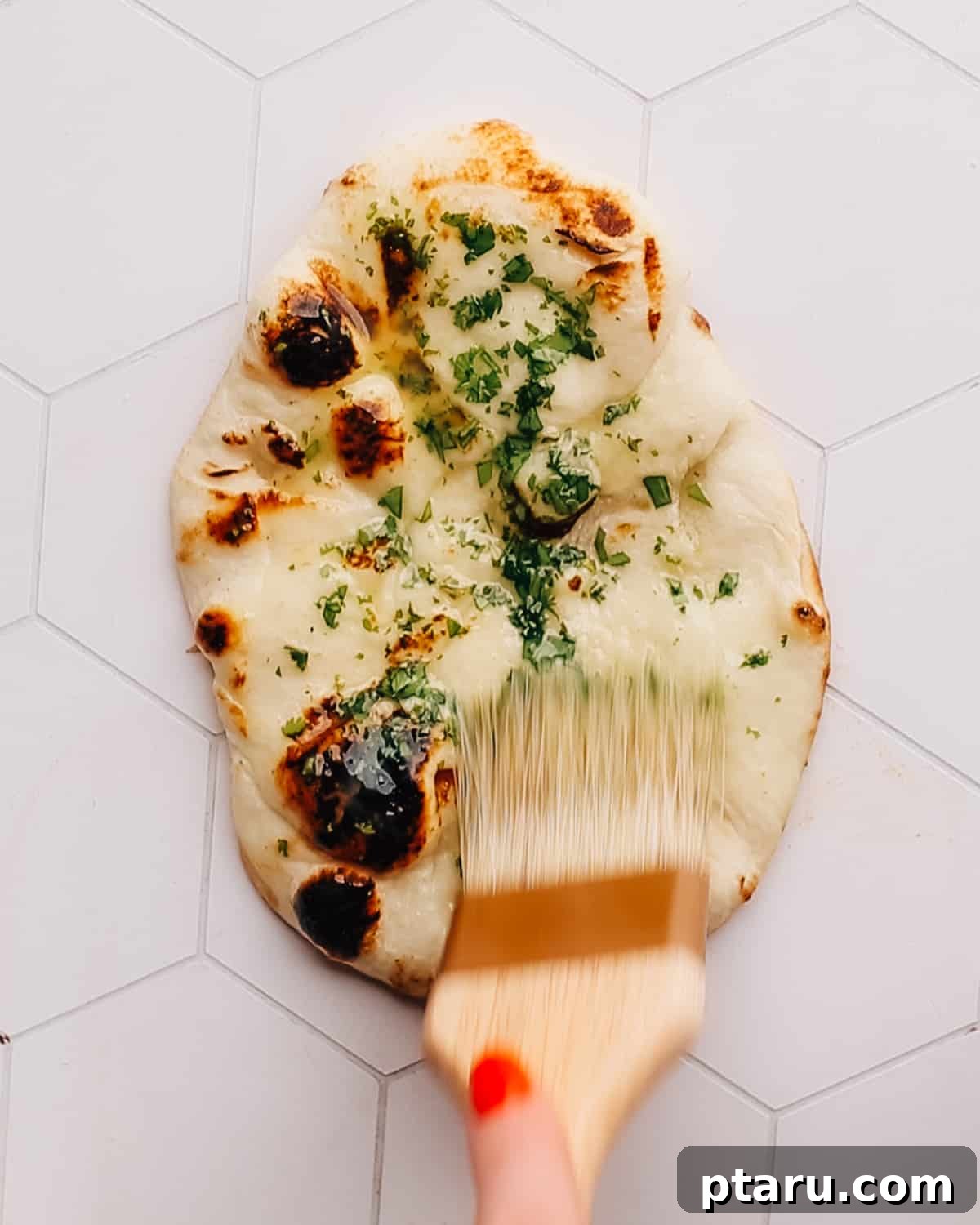 Unbelievably Soft Stretchy Garlic Naan 8 A close-up shot of a hand brushing fragrant melted garlic butter over a warm, freshly cooked garlic naan, enhancing its flavor and shine.