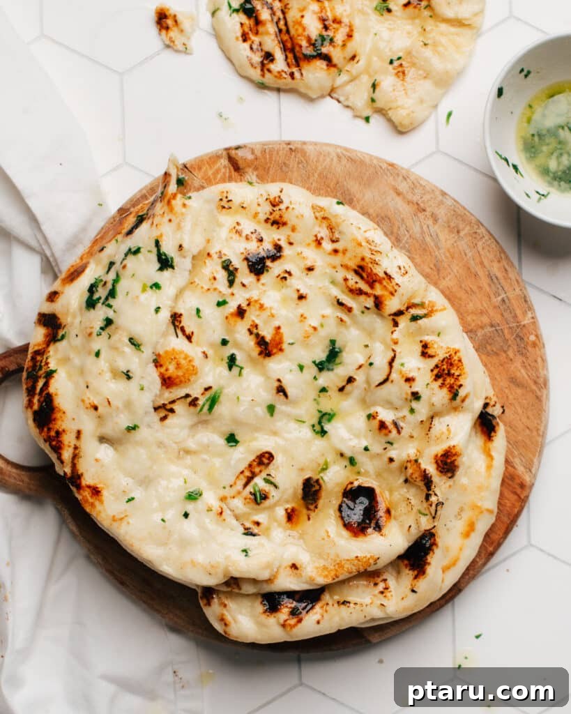 Unbelievably Soft Stretchy Garlic Naan 10 A stack of perfectly golden-brown garlic naan, fluffy and fresh, ready to be enjoyed as part of an Indian meal.