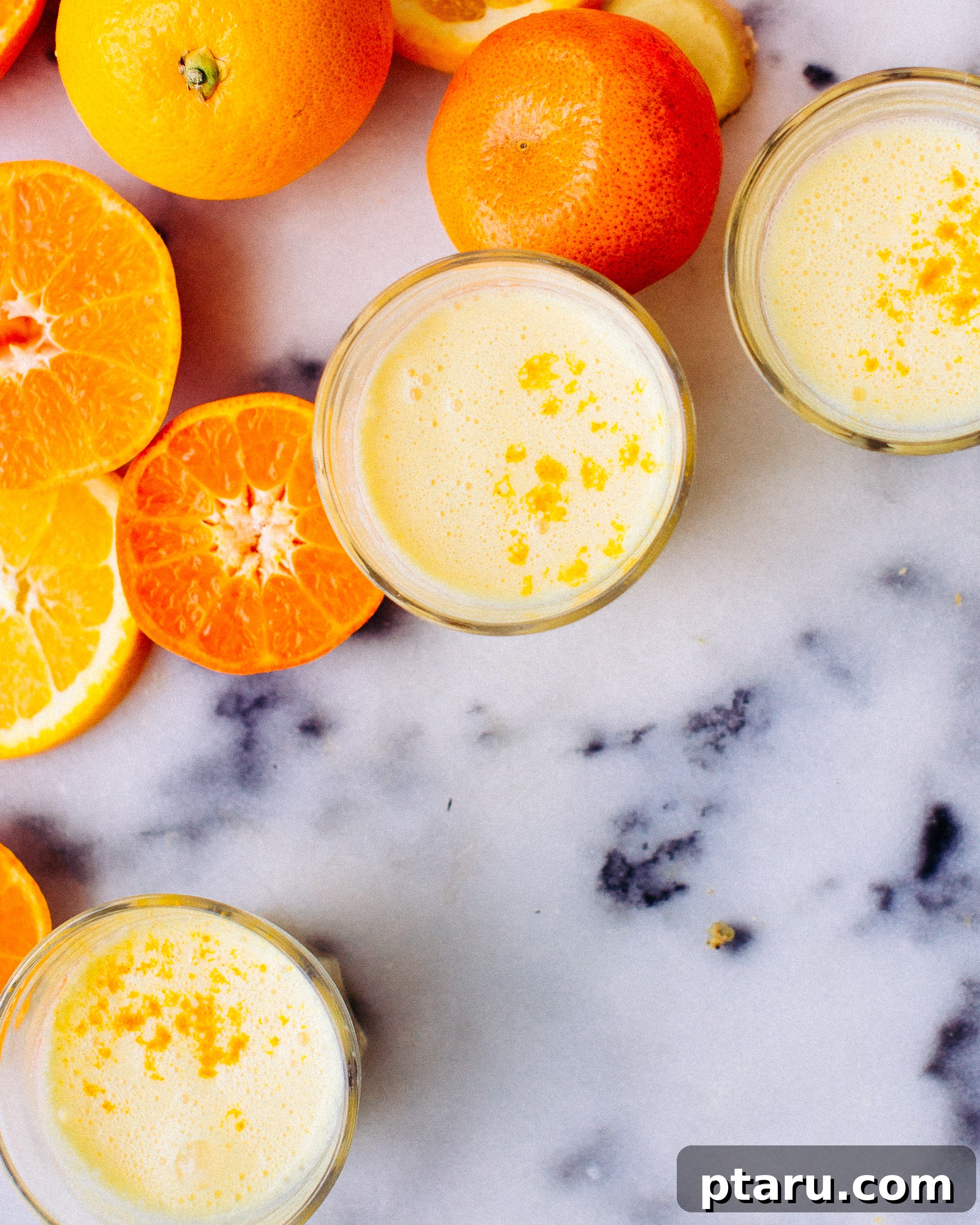 Golden Turmeric and Ginger Immune Support Smoothie 3 Hands holding a glass of the golden Turmeric and Ginger Immunity Smoothie with ingredients like orange slices and ginger in the background.