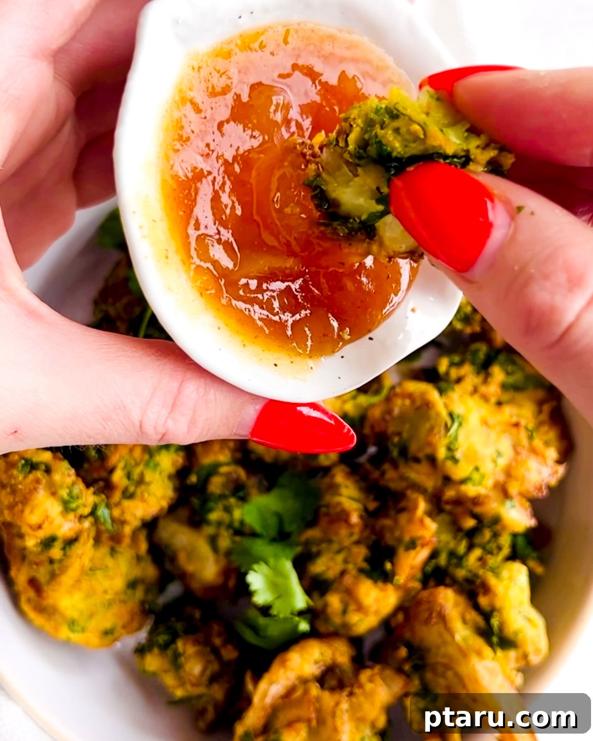 Easy Crispy Indian Pakora 7 A hand dipping a crispy pakora into a bowl of vibrant green chutney, emphasizing the perfect pairing.