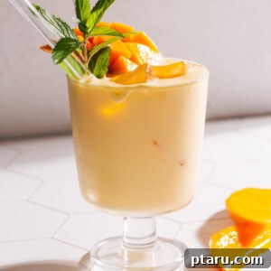 Mango lassi with a straw, mint leaves and additional mango slices.