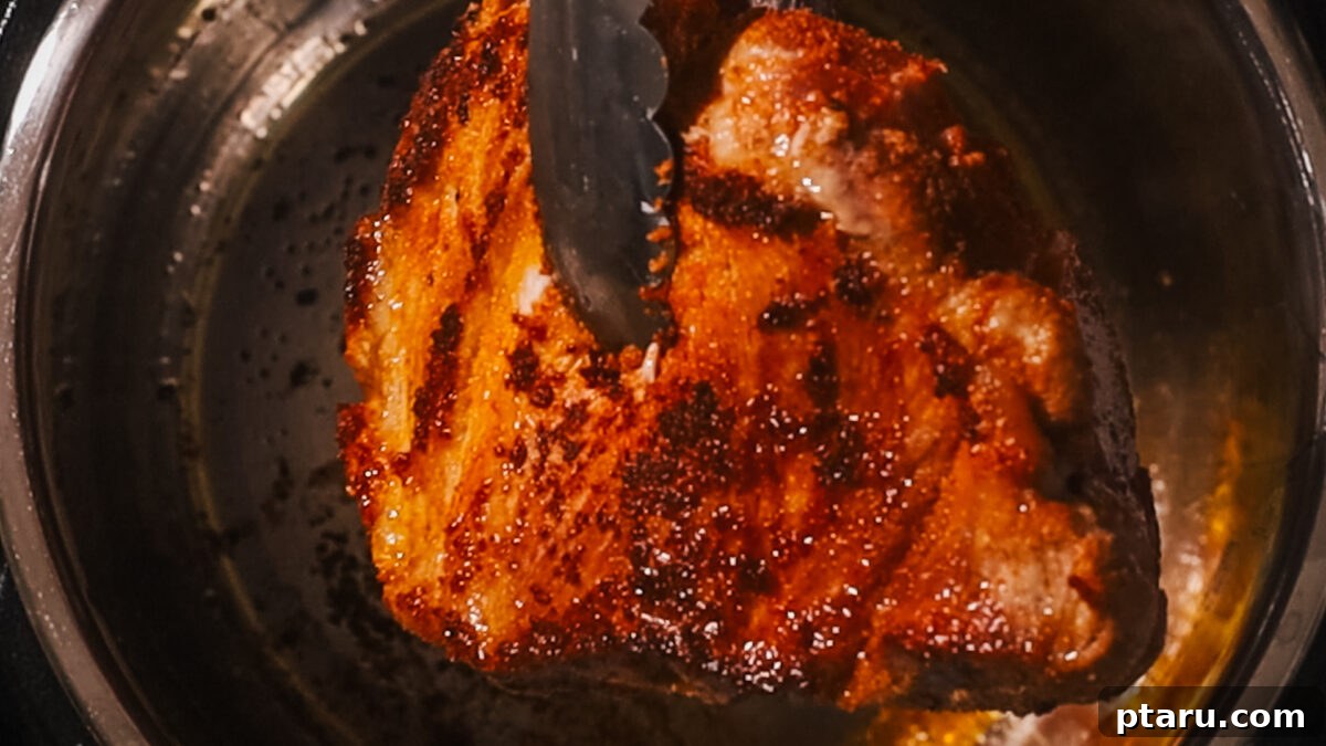 Effortless Instant Pot Fall-Apart Pulled Pork 5 Step 2: Pork searing in the Instant Pot on 'Sauté' mode, achieving a golden-brown crust on all sides.