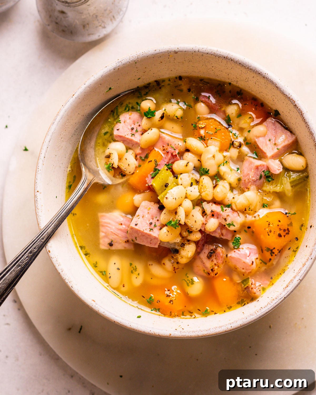 Effortless Ham and Bean Soup: Seriously Delicious and Satisfying 9 A vibrant, close-up shot of Ham and Bean Soup in a white bowl, with a spoon resting in it, showing the rich broth, tender beans, and chunks of ham.