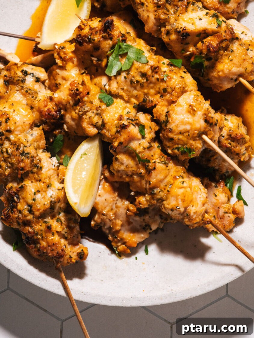 28 Plus Healthy Chicken Recipes Made Easy Delicious and Dietitian Endorsed 4 Golden brown chicken skewers on a white plate with lemon wedges and fresh herbs.