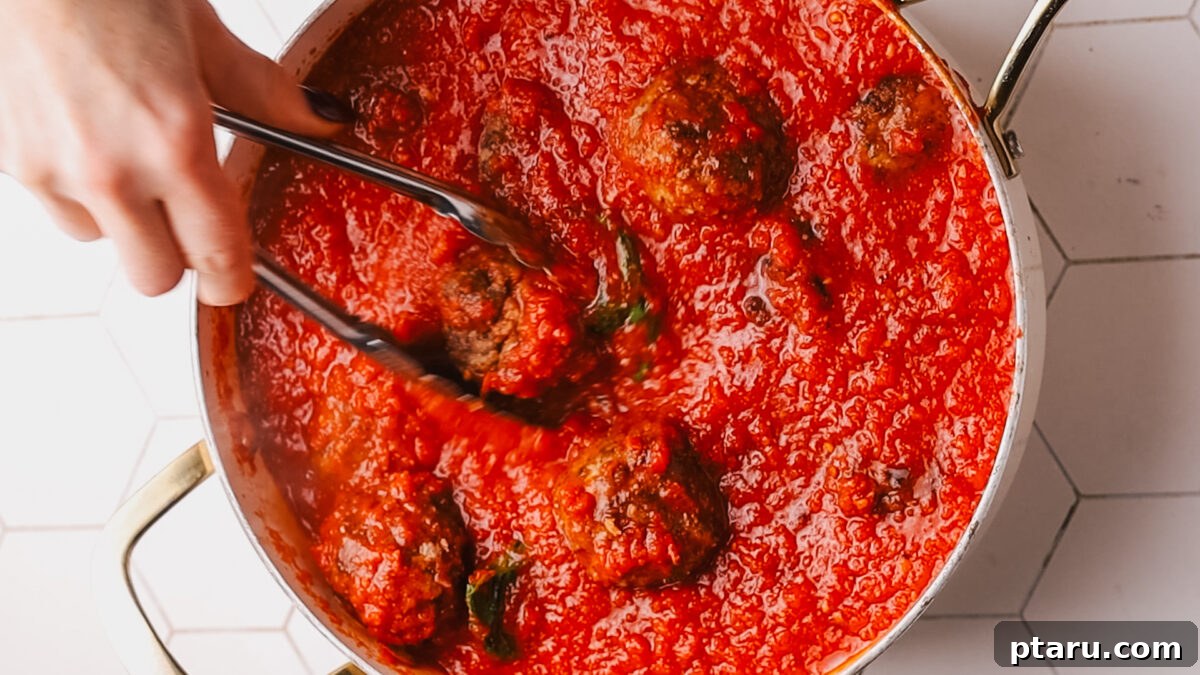 The Secret to Irresistible Meatballs 13 Meatballs simmering in rich tomato sauce in a Dutch oven.