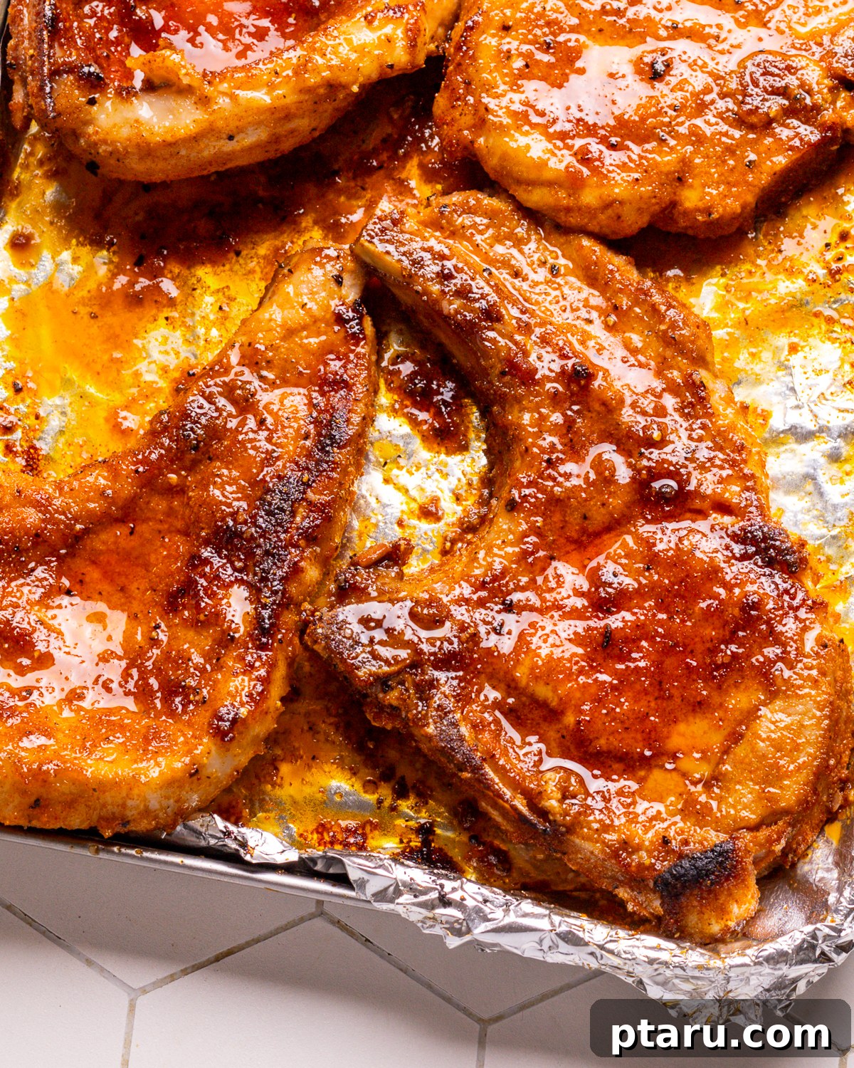 Perfect Oven Baked Pork Chops 2 Baked Pork Chops on a Foil-Lined Baking Sheet, glistening and golden.
