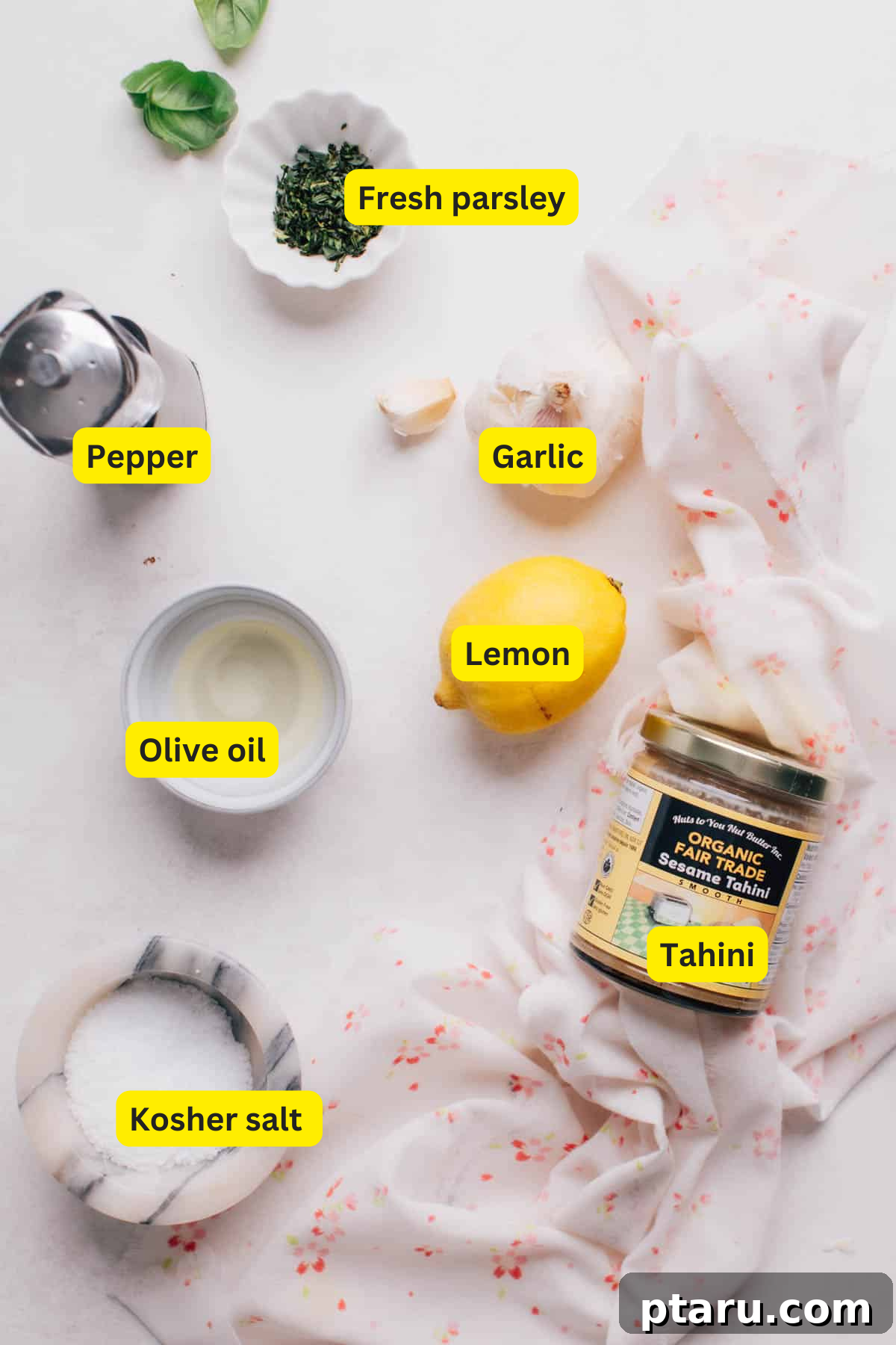 Zesty Lemon Tahini Vinaigrette 3 A collection of fresh ingredients laid out for making lemon herb tahini dressing, including lemons, tahini, olive oil, parsley, and chives.