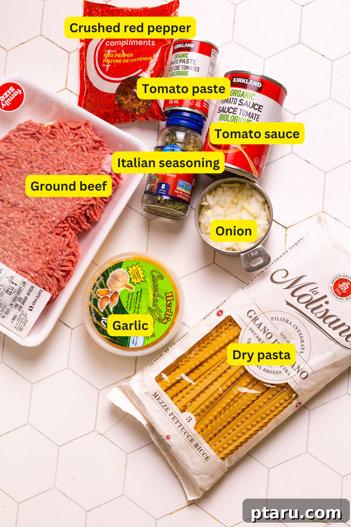 Sauce Simmered Pasta Perfection 3 A flat lay image showing all the ingredients neatly laid out for a one-pot pasta recipe, including ground beef, pasta, canned tomatoes, onion, garlic, and herbs.